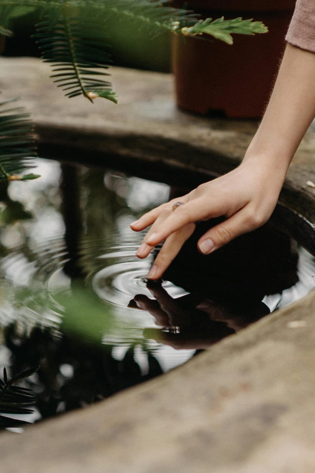 Ein Finger berührt sanft die Wasseroberfläche in einem Brunnen