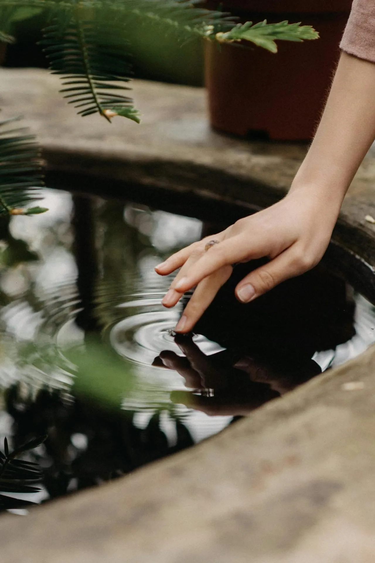 Ein Finger berührt sanft die Wasseroberfläche in einem Brunnen